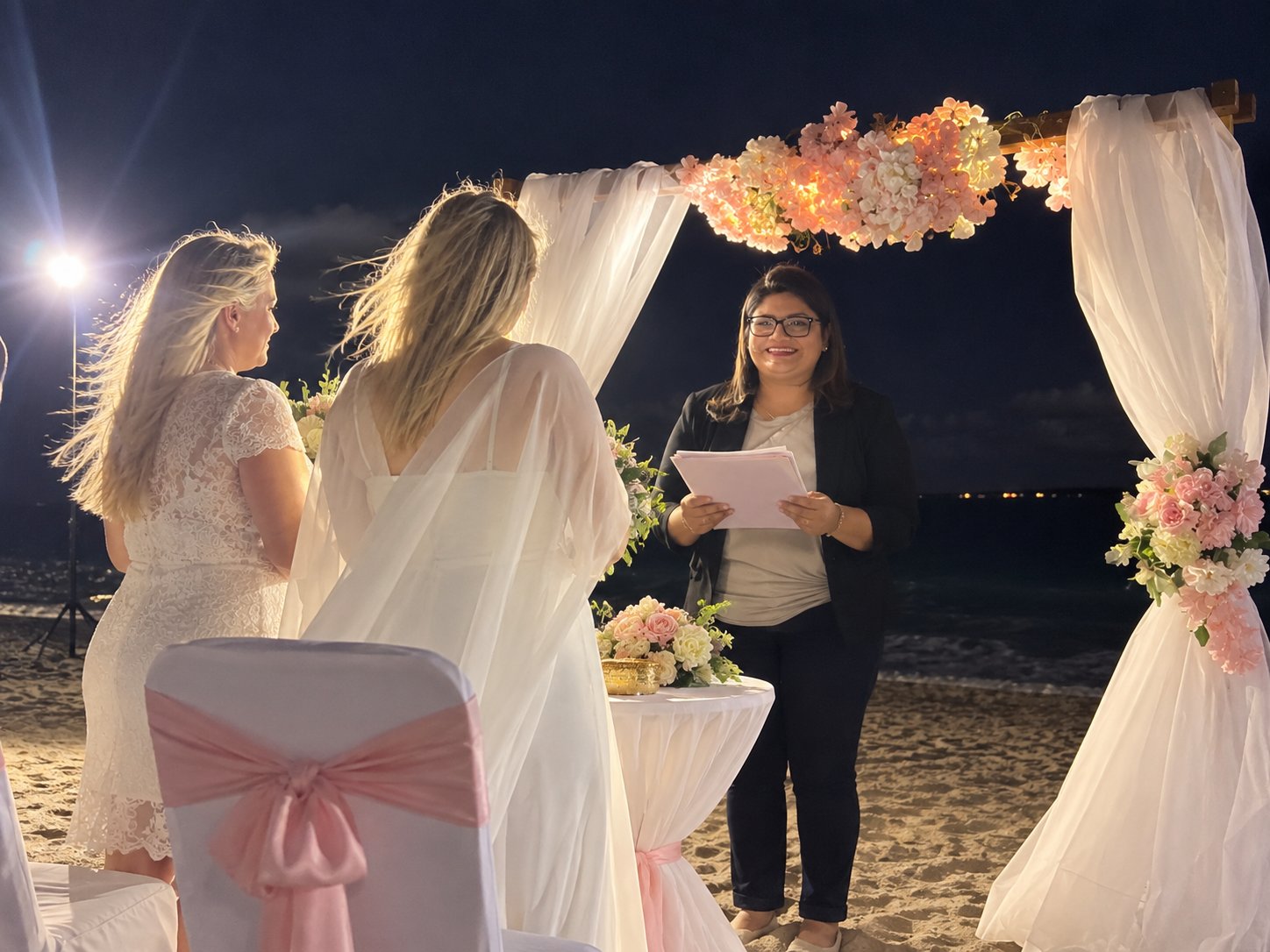 Una ceremonia nocturna en la playa bajo un arco floral